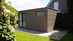 A modern house with a wooden exterior, a glass door, and a small garden area with a gravel path.