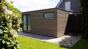 A modern house with a wooden exterior, a glass door, and a small garden area with a gravel path.