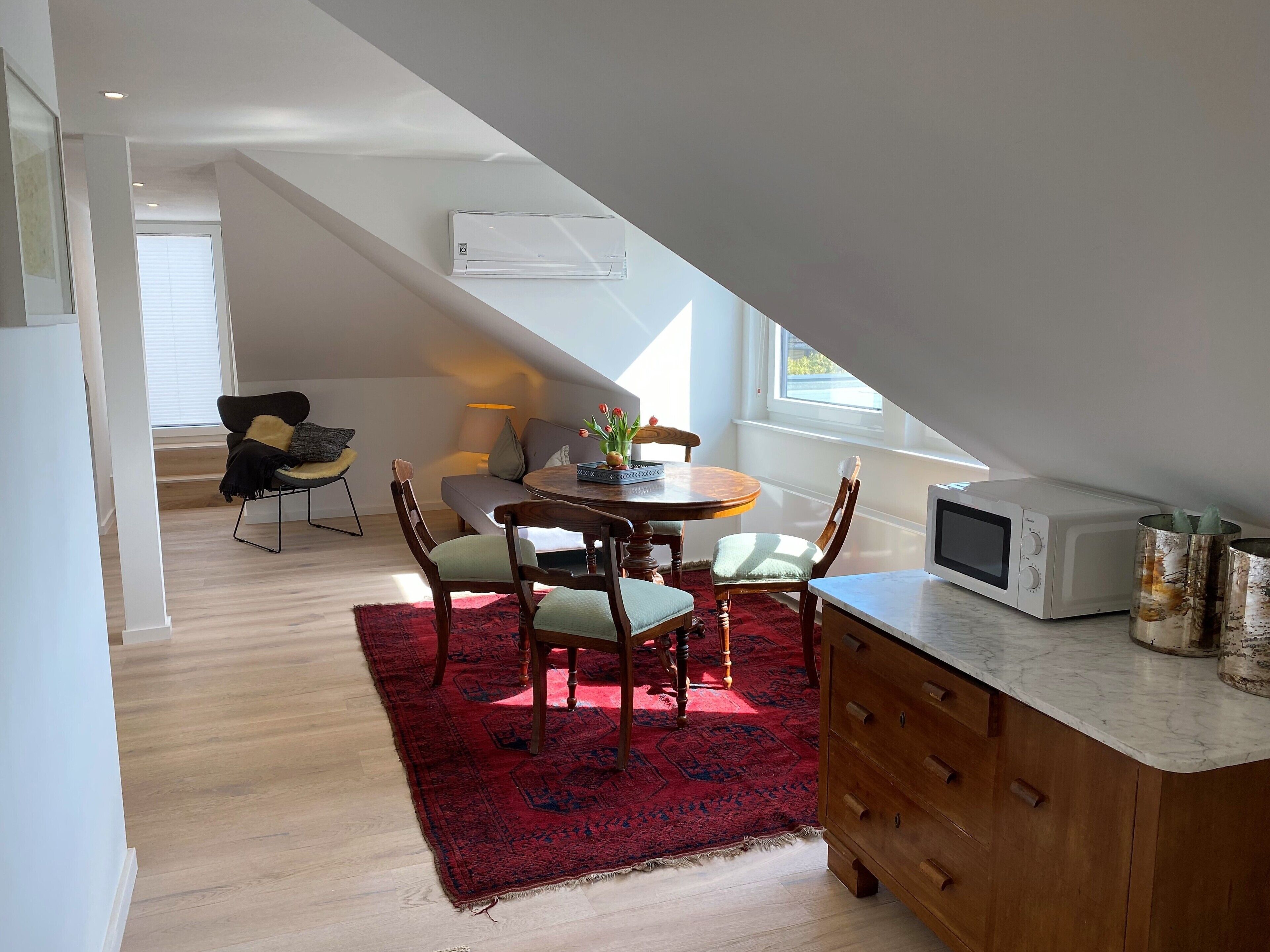 A dining area with a round table, chairs, a red rug, and a wooden cabinet.