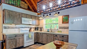 Une cuisine avec des meubles en bois, un réfrigérateur blanc, une cuisinière et une grande fenêtre qui laisse entrer la lumière naturelle.
