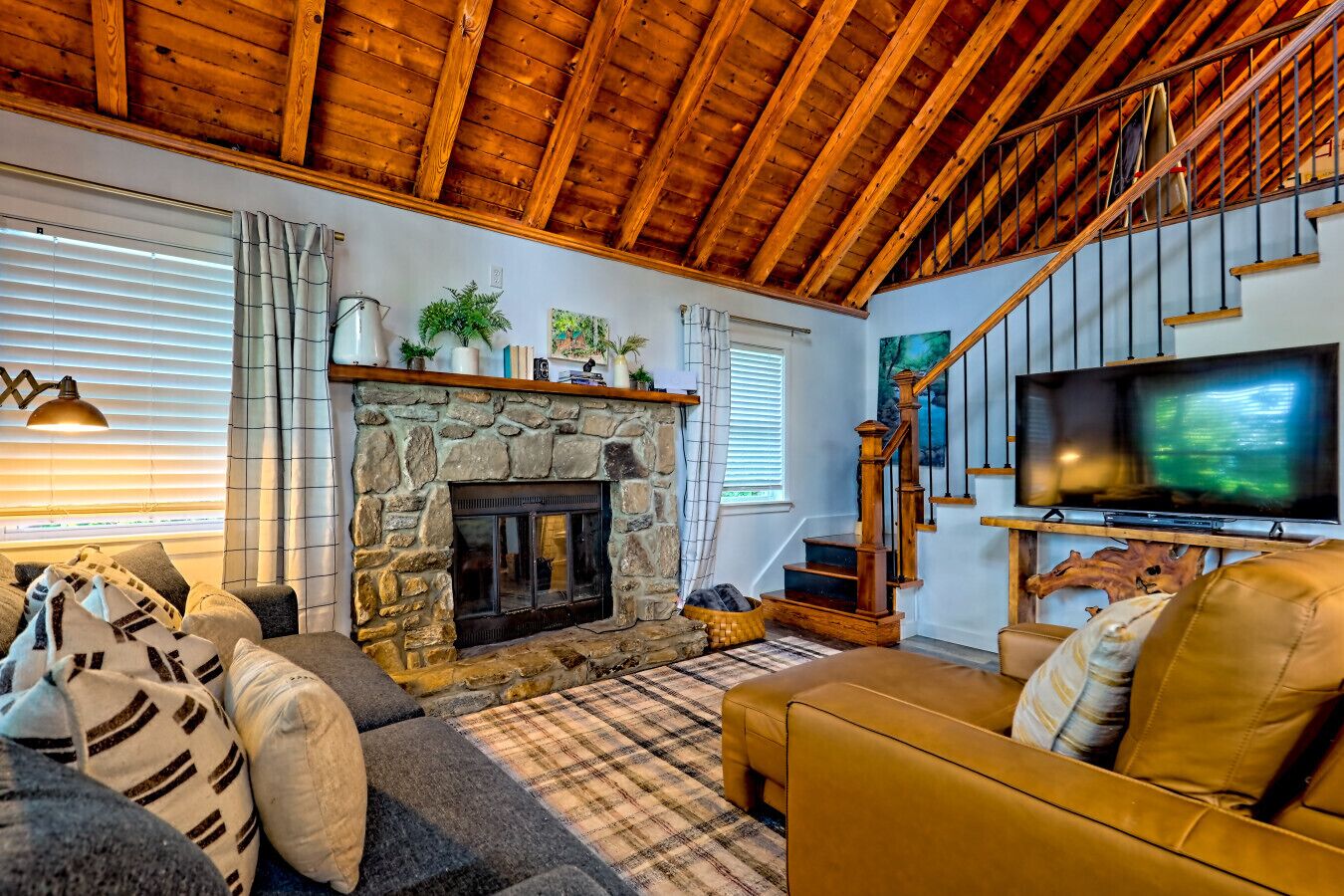 A cozy living room with a stone fireplace, a sofa, a television, and a staircase.