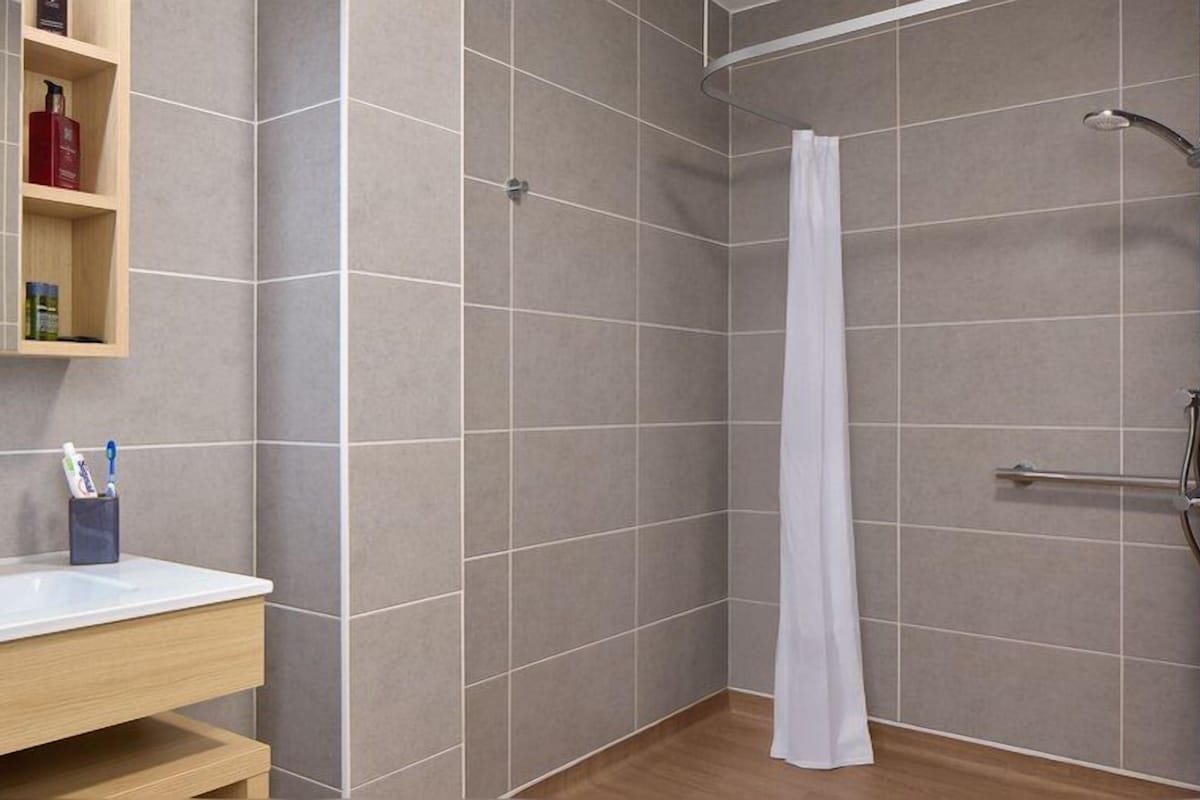 Un baño con ducha, lavamanos y repisa con artículos de aseo.