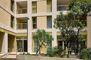 Un edificio de varios pisos con balcones, una entrada central y vegetación circundante.