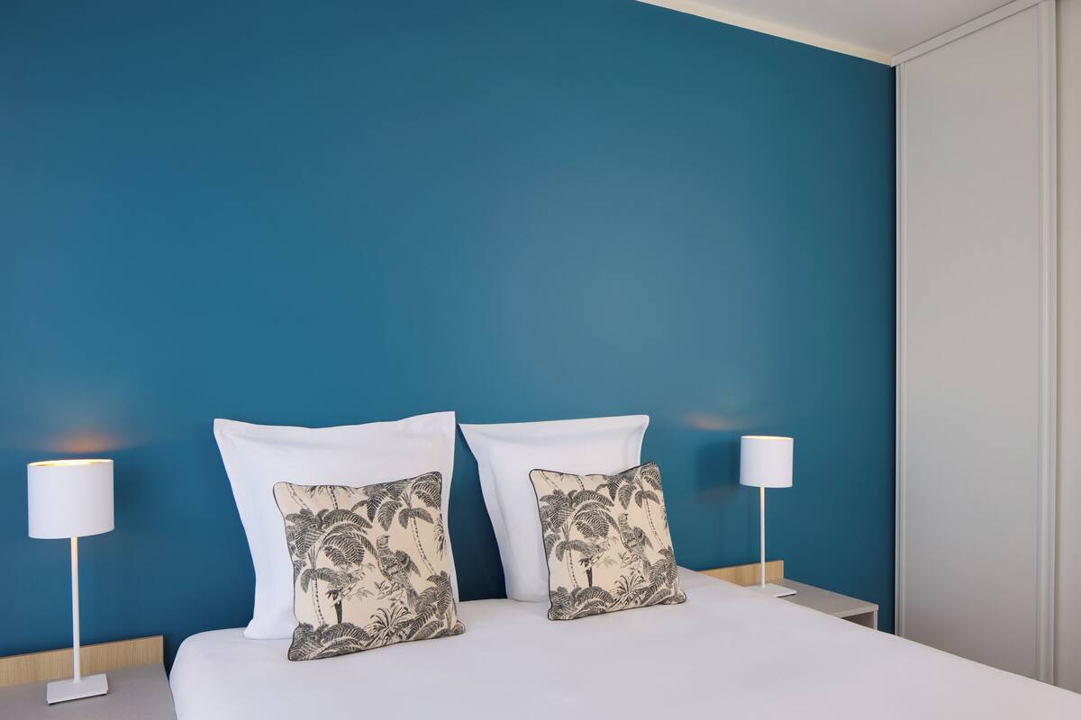 A neatly made bed with two white pillows and two matching nightstands, each with a white lamp.