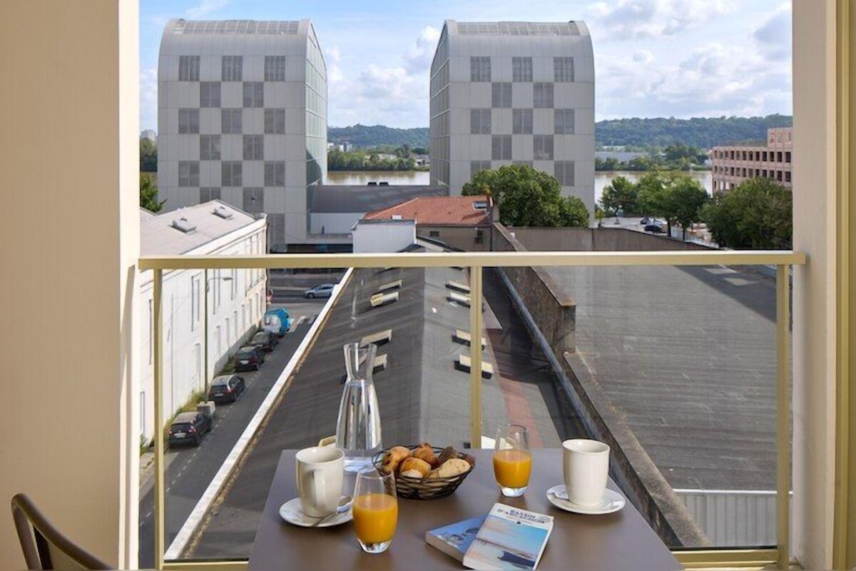A room with a view of a parking lot and buildings, a table with breakfast items, and a window with a view of the cityscape.