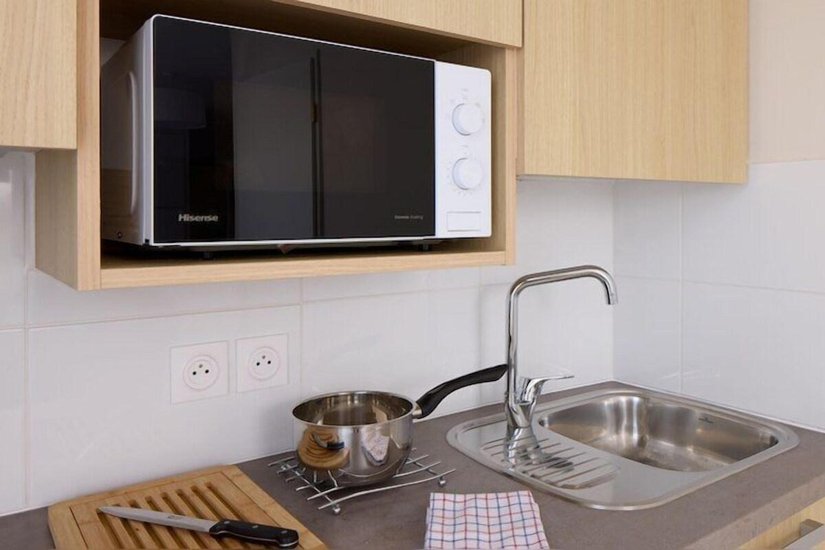 Una cocina moderna con microondas integrado, pileta de acero inoxidable y tabla de cortar de madera.