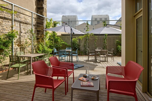 Un patio al aire libre con sillas, mesas y sombrillas rojas y verdes.