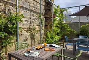 Une terrasse extérieure avec une table dressée pour le petit-déjeuner, comprenant des croissants, du café et du jus de fruits.
