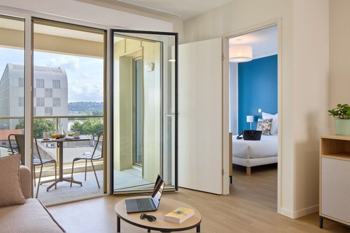Een moderne hotelkamer met balkon, een bank, een klein tafeltje met een laptop en een televisie.