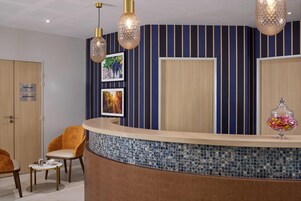 Un área de recepción con un mostrador curvo, dos cuadros enmarcados, una puerta de madera y una silla.