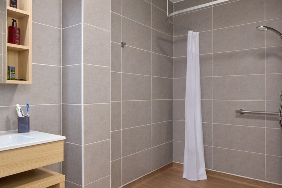 Een badkamer met een douche, een wastafel en een plank met toiletartikelen.