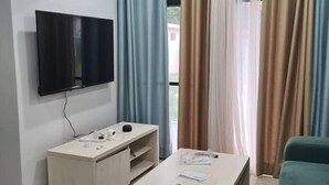 A modern living room with a flat-screen TV mounted on the wall, a wooden coffee table, a sofa, and a ceiling fan. - Aquaview Apartments (Serrekunda)