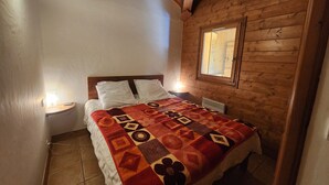 A cozy room with a wooden ceiling, a bed with a patterned blanket, a nightstand with a lamp, and a window with a view. - 4-room apartment with Wifi and parking in Samoëns (Samoëns)