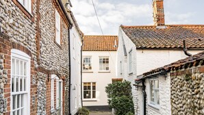 A narrow alleyway with traditional stone and brick buildings, featuring a central white building with a tiled roof and a small garden area.
