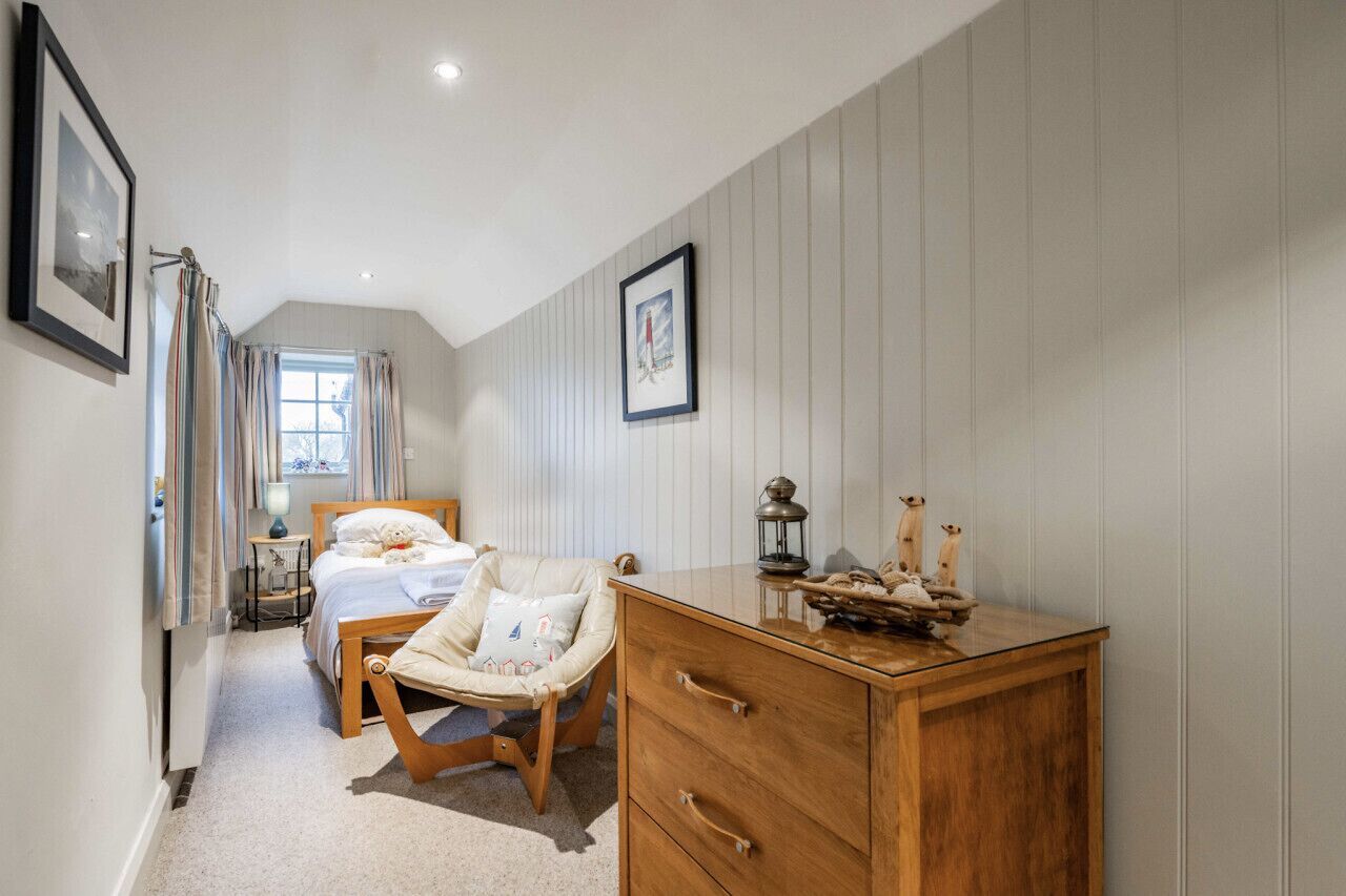 Um quarto com cama, mesa de cabeceira, cadeira e cômoda.