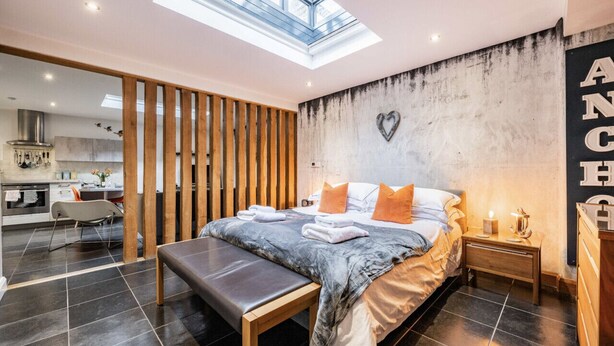 A modern bedroom with a skylight, a large bed with pillows, a bench, and a nightstand.