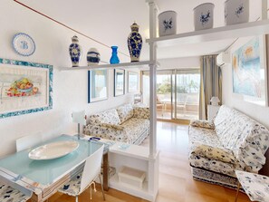A spacious living room with a glass dining table, floral-patterned sofas, and a balcony with a view.