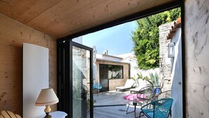 Une terrasse en bois avec une porte vitrée donnant sur un espace extérieur aménagé avec des chaises et une table.