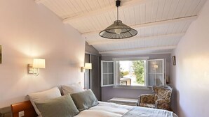 Une chambre à coucher avec un lit, deux lampes de chevet, une chaise et une fenêtre dont les volets sont ouverts.