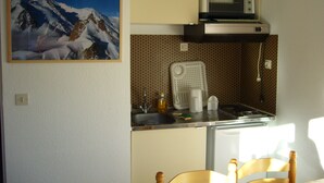 Une cuisine de taille réduite équipée d’un four à micro-ondes, d’un évier et ornée d’un tableau représentant un paysage de montagne.