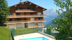 Un immeuble en bois à plusieurs étages, doté de balcons, d’une piscine et surplombant un paysage montagneux.