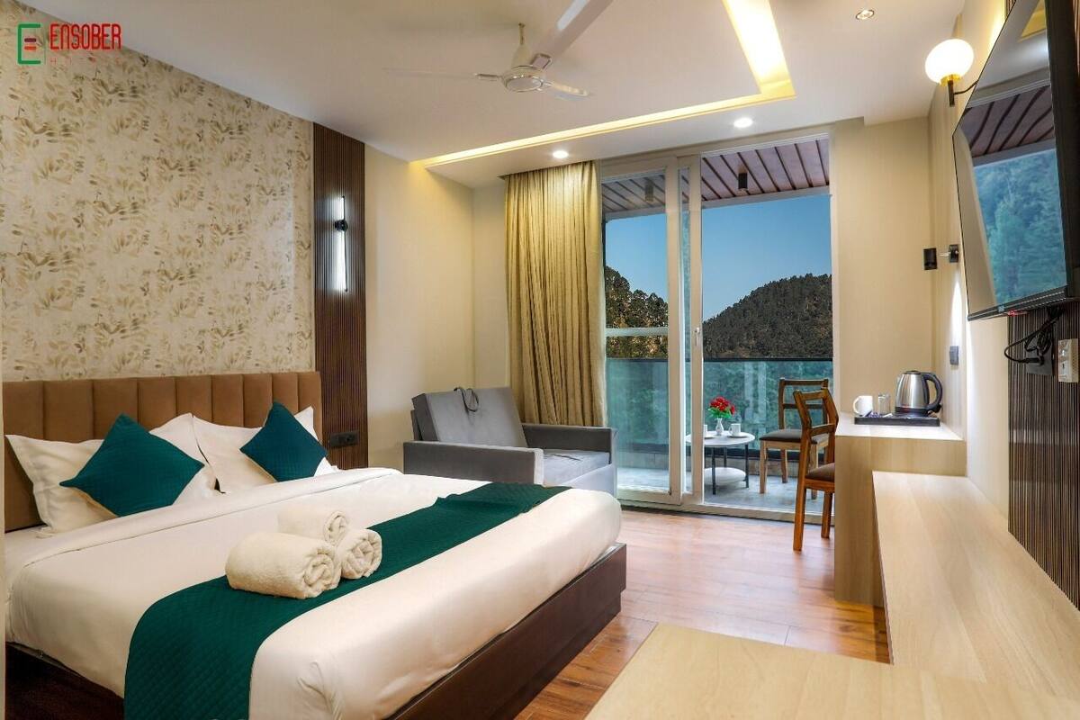 A hotel room with a large bed, a sofa, a dining area, and a balcony with a view.