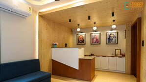 A reception area with a wooden reception desk, a blue sofa, and framed pictures on the wall. - Vinsober Kainchi Dham Nainital  (Kosiyakutoli)