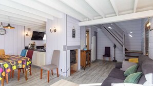 A spacious living area with a sofa, a dining table with chairs, a fireplace, and a staircase leading to another level.