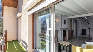 A modern interior with a glass door leading to a balcony with artificial grass, a fireplace, and a seating area with yellow chairs.