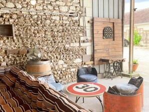 A rustic outdoor seating area with stone walls, a dartboard, and a speed limit sign. - Family cottage with private terrace near Beauval (Meusnes)