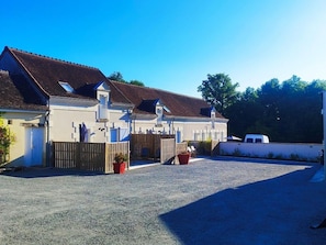 A row of white buildings with brown roofs, a gravel driveway, and a white van parked to the right.