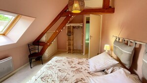 A bedroom with a sloped ceiling, a bed with floral bedding, a chair, a bedside lamp, and a wooden ladder leading to a lofted area. - Family cottage with private terrace near Beauval (Meusnes)