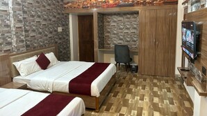 A hotel room with two beds, a desk, a TV, and a mural of a cityscape on the wall. - Atithi Palace Luxury Guest House (Varanasi)