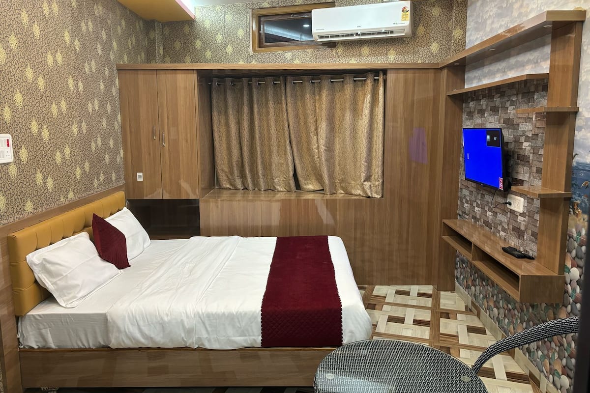 Un dormitorio con cama, televisión, aire acondicionado y ventana con cortinas.