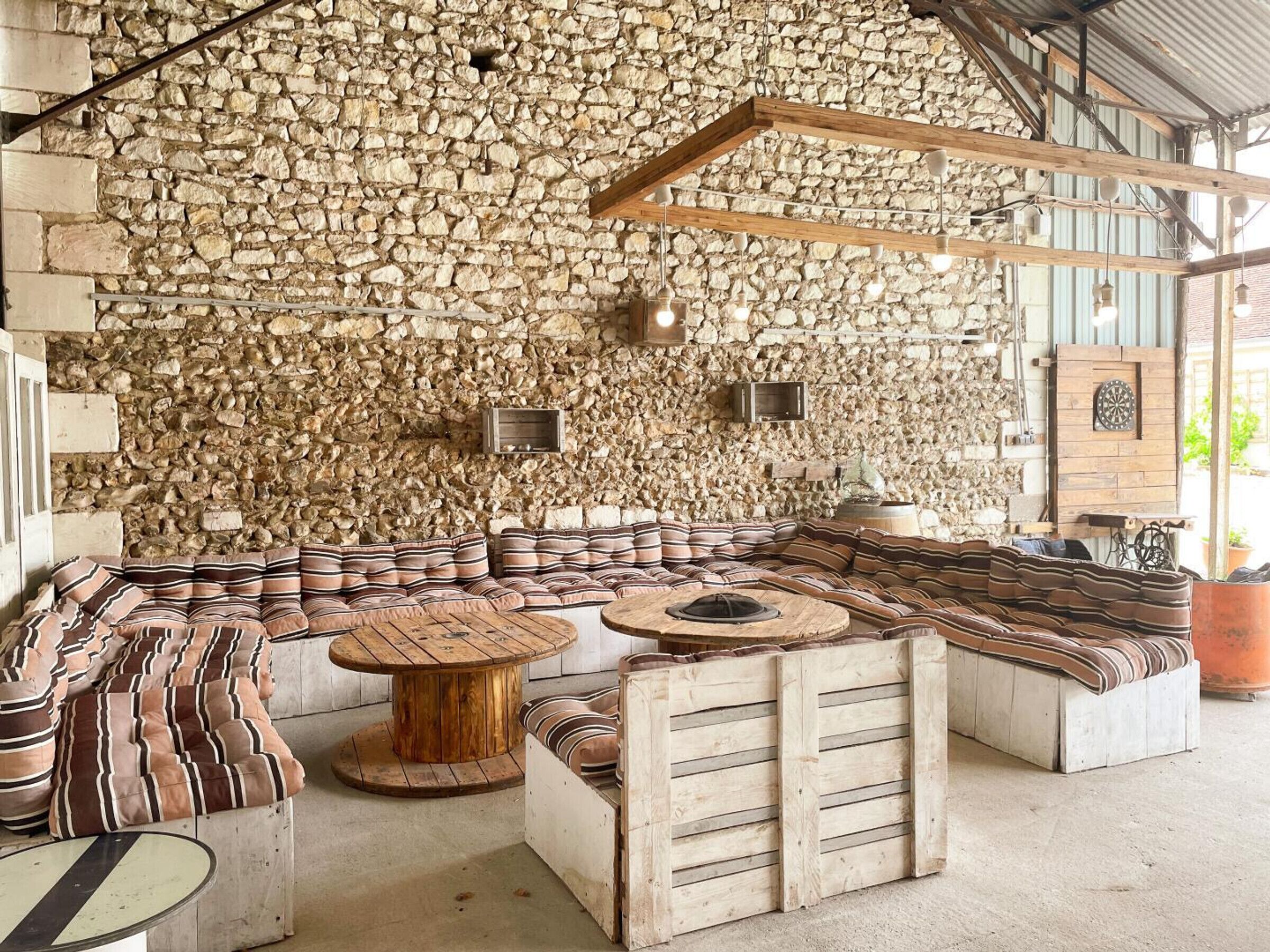 A rustic stone wall interior with a curved seating area, wooden tables, and a dartboard.