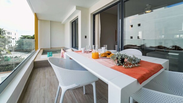 A balcony with a dining table set for two, featuring a glass of orange juice, croissants, and a vase with flowers. - Beautiful new apartment steps from the beach (Punta Cana)