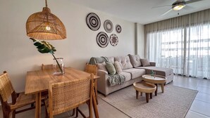 A modern living room with a dining area, a sofa, a ceiling fan, and decorative wall art. - Beautiful new apartment steps from the beach (Punta Cana)