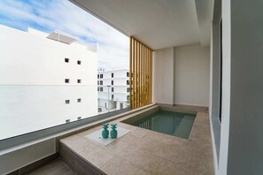 A modern balcony with a built-in hot tub, a view of the city, and a wooden privacy screen. - Beautiful new apartment steps from the beach (Punta Cana)