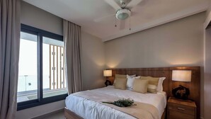 A modern bedroom with a large bed, wooden headboard, bedside lamps, and a view of a balcony. - Beautiful new apartment steps from the beach (Punta Cana)