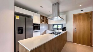 A modern kitchen with a central island, built-in appliances, and a wooden door. - Beautiful new apartment steps from the beach (Punta Cana)