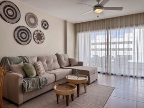A modern living room with a beige sofa, two wooden side tables, and decorative wall art. - Beautiful new apartment steps from the beach (Punta Cana)