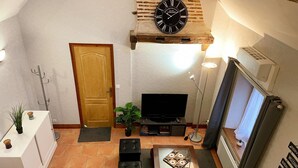 A living room with a television, a wooden door, a plant, and a clock on the wall. - Charming house for 4 people in Tour-en-Sologne, with air conditioning (Tour-en-Sologne)