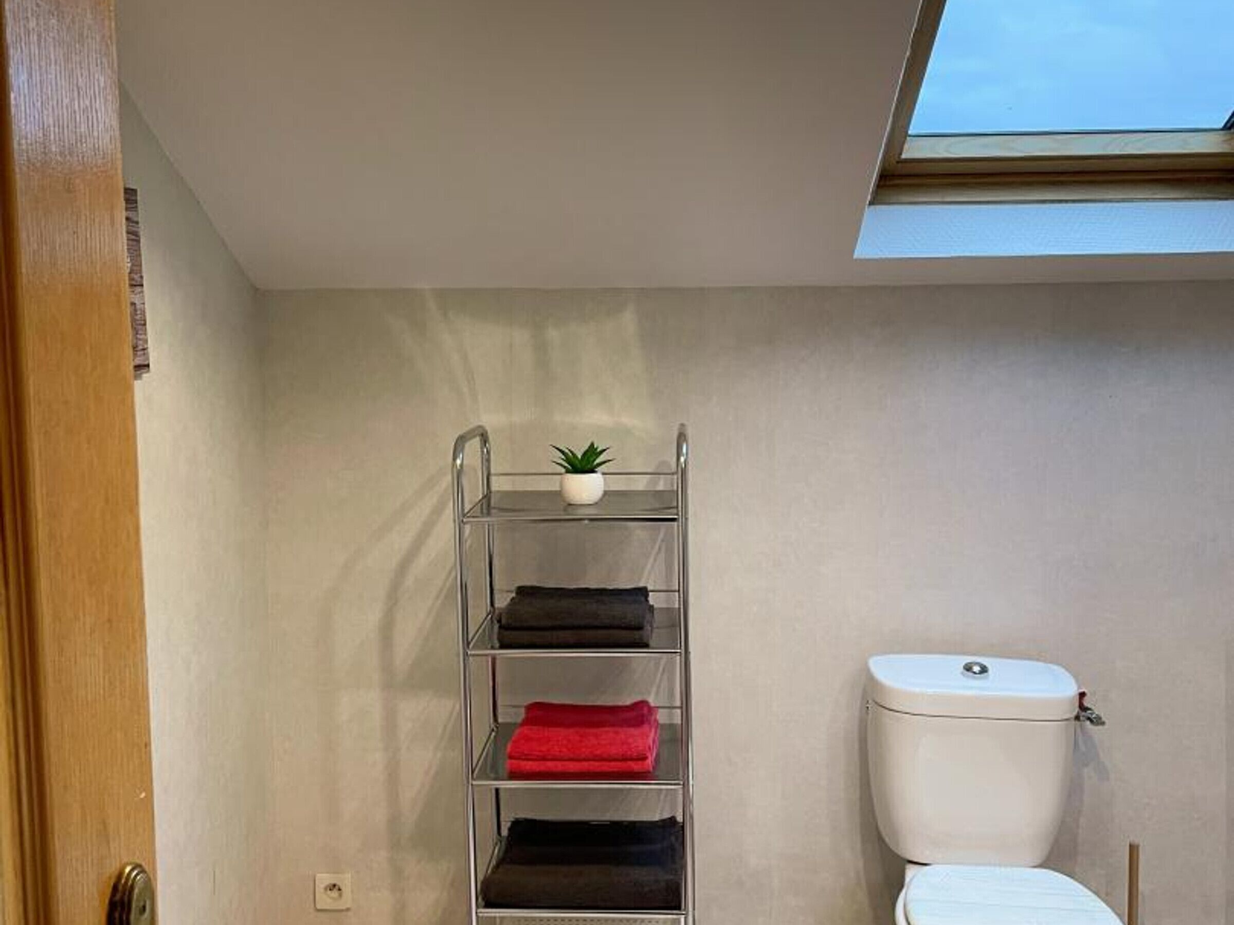 Et badeværelse med ovenlys, et hvidt toilet og en metalkasse med sammenfoldede håndklæder.