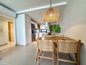A modern kitchen with white cabinets, a stainless steel refrigerator, and a dining area with a wooden table and wicker chairs. - Spectacular PH w private rooftop steps from beach (Punta Cana)