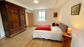 Une chambre à coucher comprenant un lit, une armoire en bois, une fenêtre et une table de chevet avec une lampe.