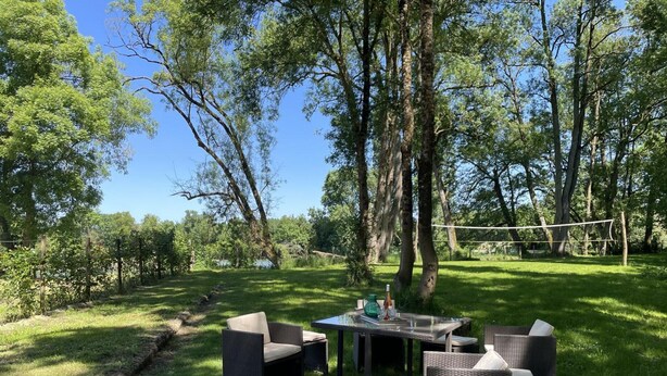 Un espace extérieur aménagé avec des meubles en osier et une table, entouré d’arbres et d’une pelouse verdoyante.