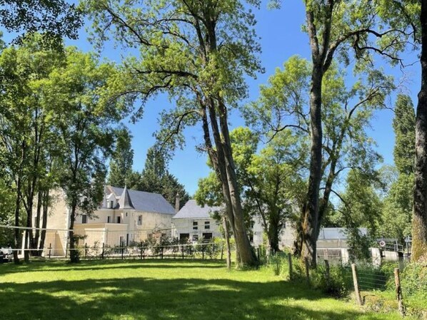 A large building with multiple windows and a sloped roof, surrounded by lush green trees and a well-maintained lawn.