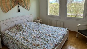 A bedroom with a bed, a bedside table, a lamp, a chair, and two windows.