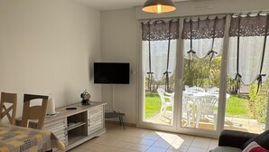 A living room with a TV, a dining table, chairs, a sofa, and a sliding glass door leading to an outdoor patio.