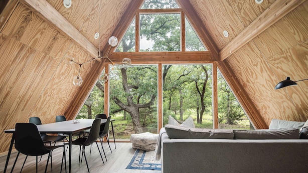 A cozy, wooden-paneled room with a dining area, a sofa, and large windows offering a view of the forest. - Large A-Frame in Nature - minutes from Main (Fredericksburg)